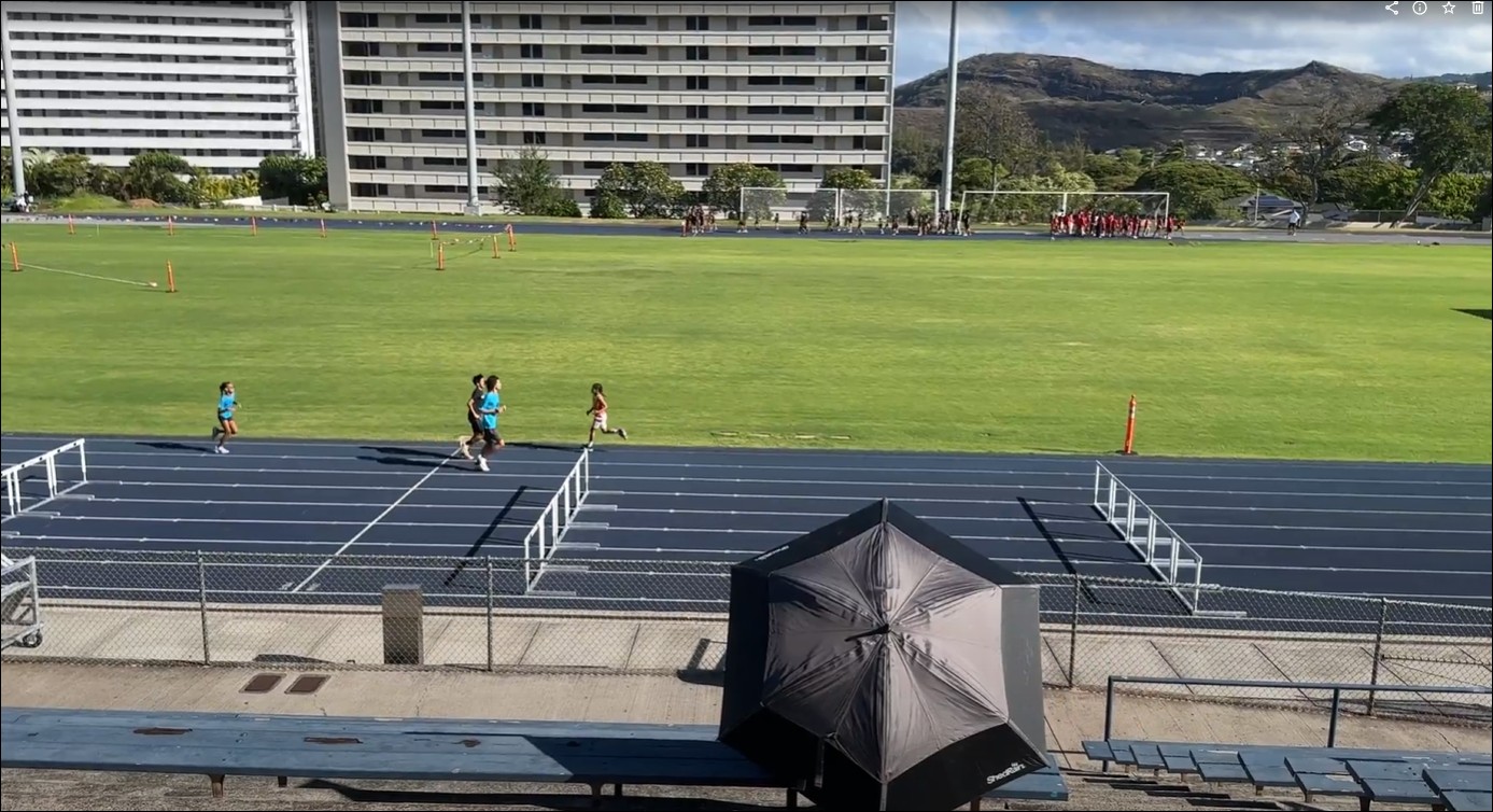 Parent sitting under an umbrella at a track meet