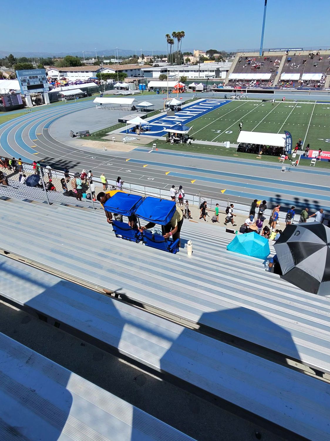 Bleacher view showing portable stadium seats with blue canopies providing shade