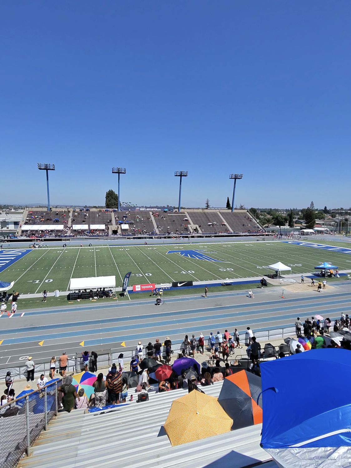 Spectators using UV umbrellas and shade canopies in the bleachers at a track meet