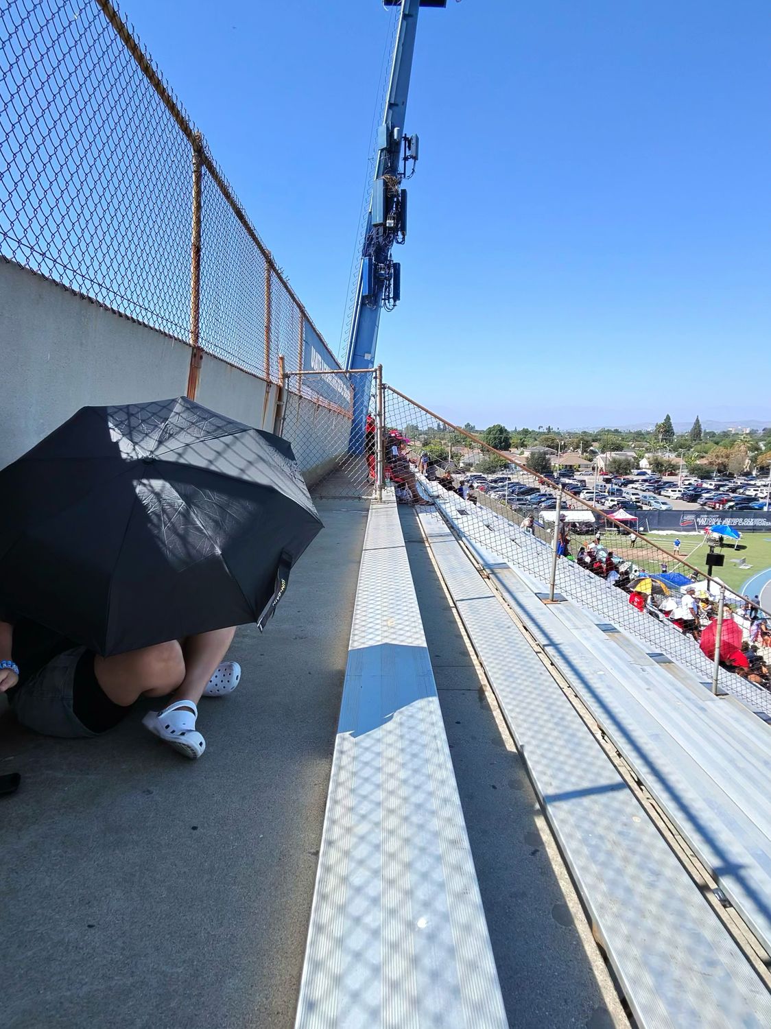 Spectator using a UV umbrella for shade on hot metal bleachers at Cerritos College